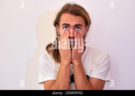 A closeup shot of a young attractive man with blue eyes and a beard touching his face Stock Photo