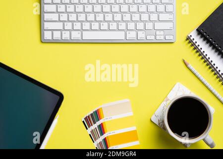 Graphic designer office table view with tablet, color guide palette, keyboard, paper notebooks on yellow background. Creative professional workspace, Stock Photo