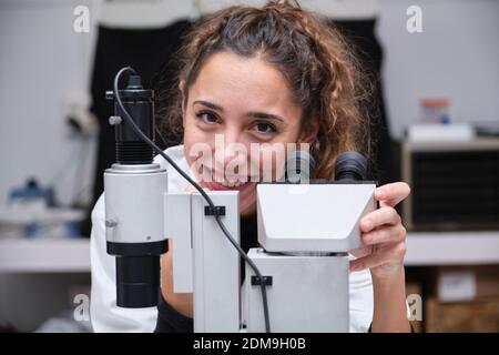Young female scientist looking at camera and smiling next to a microscope in a laboratory. Laboratory research concept. Stock Photo