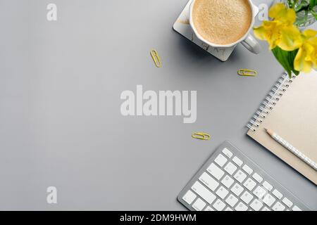 Minimal style workspace with coffee cup, paper notebook, pencil, yellow flower and stationery on grey background. Modern office desk table top view. B Stock Photo