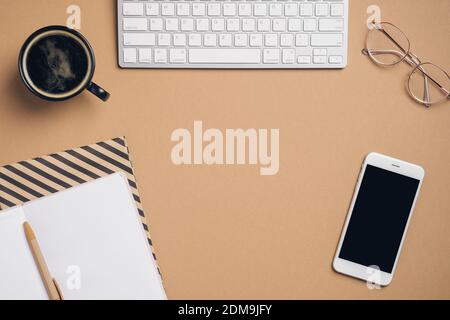 Flatlay computer keyboard, cup of coffee, glasses, phone with blank screen mockup, paper notebooks on pastel beige background. Elegant feminine worksp Stock Photo