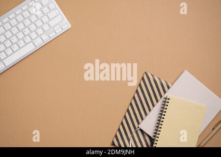 Home office desk top view with keyboard, paper notebooks, notepad, pen on beige background. Flat lay, view from above. Elegant feminine workspace with Stock Photo