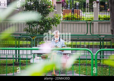 As the pandemic is still on-going, Singaporeans are very discipline to wear a mask, here is an old man wearing a mask sitting in the public park area. Stock Photo