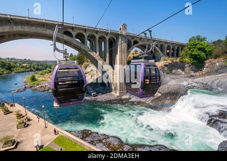 Two gondolas fly over the Spokane River and falls near Riverfront Park on a summer day in Spokane, Washington, USA Stock Photo