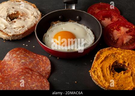 A balanced breakfast or snack on black wood for one person: a sesame bagel toasted and sliced in half with pub cheese and cream cheese on, slices of t Stock Photo