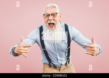 Senior man having fun posing in front camera - Happy mature male enjoying retired time - Elderly people lifestyle and hipster culture concept - Pink background