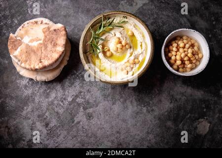 Home made hummus bowl, decorated with boiled chickpeas, herbs, pita and olive oil over a rustic metal background. Top View.