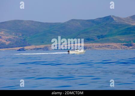 The white boat sails on a calm blue porch against the backdrop of the islands. Motor boat trips Stock Photo