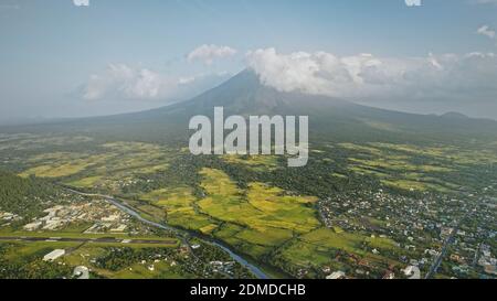 Volcano erupt at countryside cityscape aerial. Urban cottages with traffic road at green valley. Legazpi city at Mayon mount landscape, Philippines, Asia. Cinematic tourist attraction at mist haze Stock Photo