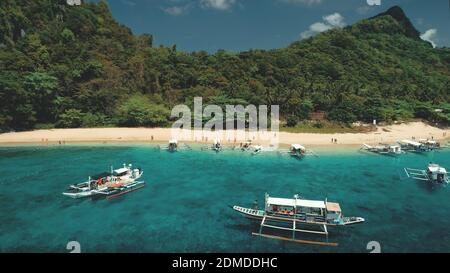 Ocean harbor with traditional passenger boats at sand beach. Epic tropical cruise with resting people at shore of El Nido Islands, Palawan, Philippines, Asia. Green forested mount landscape. Stock Photo