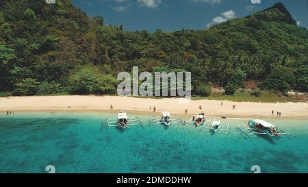 Tropical cruise with resting people at ocean shore aerial. Epic harbor with traditional passenger boats at sand beach of El Nido Islands, Palawan, Philippines, Asia. Green forested mount landscape Stock Photo