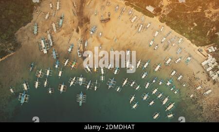 Pier top-down aerial with water transport at sun set soft light. Ocean sand coast with green trees at beach. Ships, vessels, boats, yachts at shallow coastal waterfront. Cinematic top down shot Stock Photo