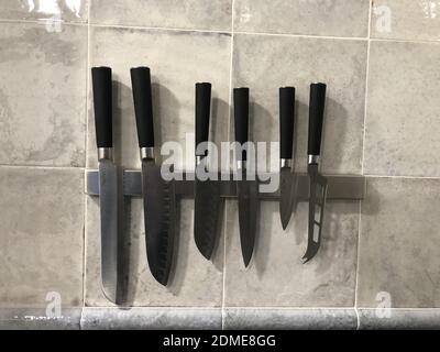 A closeup shot of a magnetic holder with sharp knives on a kitchen til Stock Photo
