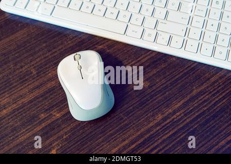 A white computer mouse and keyborad on a wooden desk of an office. Stock Photo