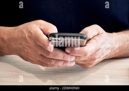 Businessman holds a mobile phone or smartphone in his hand and texting a message on a wooden office desk Stock Photo