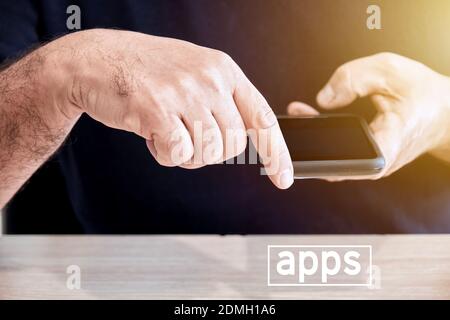 Male person holds a mobile phone or smartphone in his hand with his finger pointing towards the word apps. To download or to use applications in smart Stock Photo
