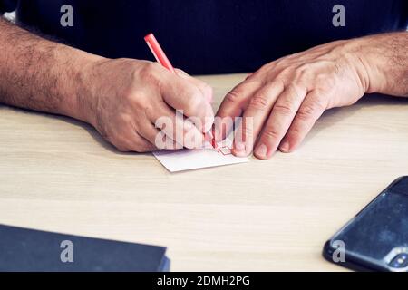 Hand of a male businessman holding a pen and taking notes on a note paper on a wooden desk. Stock Photo