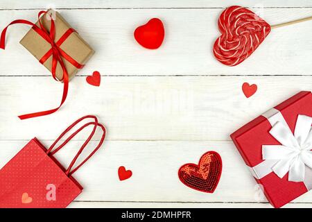 Creative Valentine Day romantic composition with red hearts, satin ribbon, lollipop, gift box and paper bag on white background. Mockup with copy spac Stock Photo