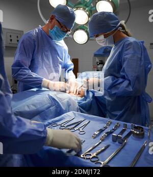 Medical team in surgical suits performing aesthetic surgery in operating room. Doctors in sterile gloves and protective masks doing cosmetic surgery. Concept of plastic surgery. Stock Photo