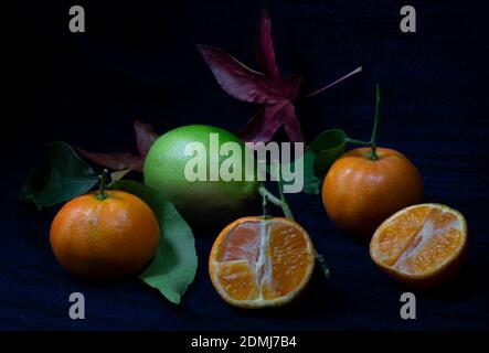 Tangerine whole and open-face with lemon and maple leaf on dark background Stock Photo