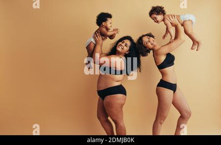 Two women holding their babies up. Woman postpartum bodies. Real body of a healthy mothers with their kids. Stock Photo