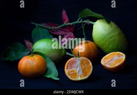 Tangerine whole and open-face with lemon and maple leaf on dark background Stock Photo