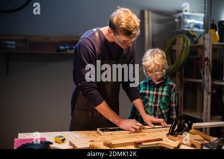 an experienced carpenter and his young apprentice make wood crafts in their workshop Stock Photo