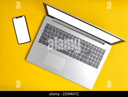Laptop and frameless phone on a yellow background. Modern technological gadgets, white screens for copy space Stock Photo