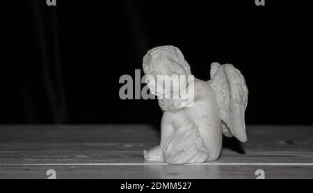 Small angel with wings on a black background, free space for text. Concept of memory of a person, funeral. Stock Photo