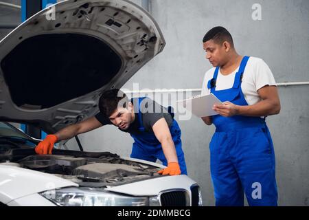 Two mechanics inspect the engine of a car and discuss repair Stock Photo