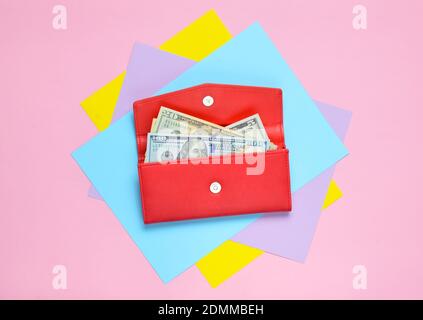 Red leather purse with dollar bills on a colored pastel background. Top View Stock Photo