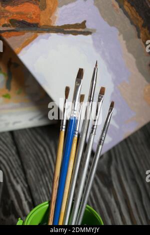 Paint by number brushes. Nearby is a fragment of a painted picture. On black pine boards. Stock Photo