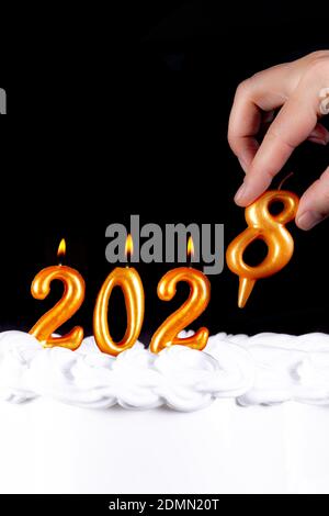 Four golden candles write numbers flame happy new year 2028 hand black background Stock Photo