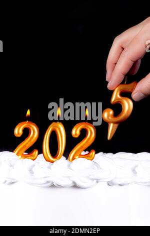 Four golden candles write numbers flame happy new year 2025 hand black background Stock Photo