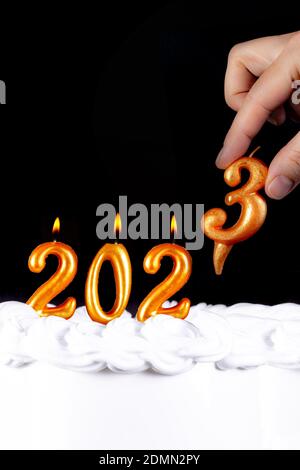 Four golden candles write numbers flame happy new year 2023 hand black background Stock Photo