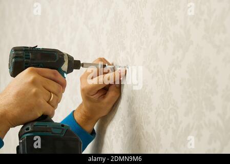 home worker drives the screw into the concrete wall using electric screw driver. Stock Photo