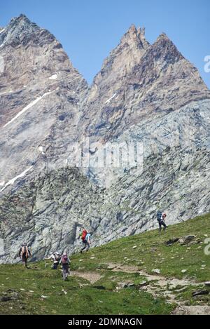 Beautiful view of large pyramidal peaks with hikers team. Male mountaineers walking uphill while hiking in mountains. Concept of travelling, hiking and mountaineering in Alps. Stock Photo