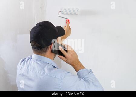 Painting a drywall by painting roller and white latex color. Stock Photo