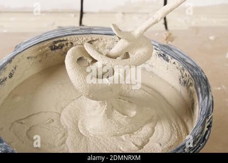 the master mixes the plaster in a bucket. Flat house renovation, master mixed the mortar in a plastic bucket with mixer Stock Photo