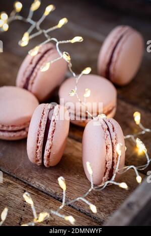 Fig macarons beautifully arranged on a wooden plate , winterly decorated with fir branches and pine cones, a LIchter chain glows in the background Stock Photo