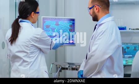 Scientist team arguing in front of computer looking at virus development in modern equipped laboratory. Multiethnic stuff analysing vaccine evolution using high tech for researching treatment. Stock Photo