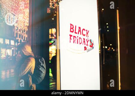 Black Friday signage on digital OOH display with unrecognizable man talking on the smartphone and Christmas decorations in background Stock Photo