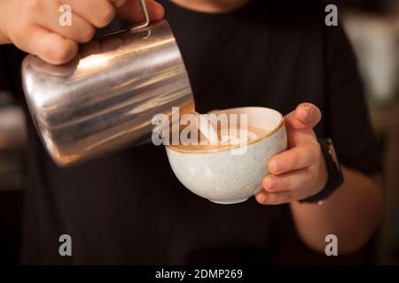 Cropped close up of a barista pouring hot milk into coffee cup, preparing delicious cappuccino Stock Photo