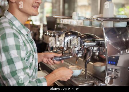 Cropped shot of a cheerful male barista smiling, using coffee machine, preparing drink for a customer Stock Photo