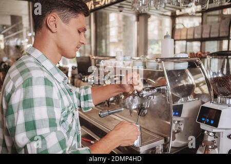 Male barista using coffee machine, making a cup of coffee for his customer. Young man working at the coffee shop. Employment, profession concept Stock Photo