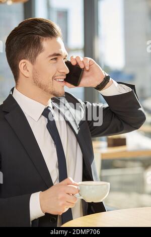 Good news. Vertical shot of a handsome businessman enjoying his coffee talking on the phone smiling happily Stock Photo