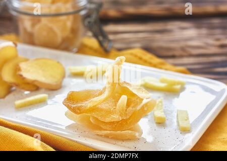 Candied ginger slices in a white plate on wooden table. Dehydrated oriental fruits. Healthy sweets. Antioxidants Stock Photo