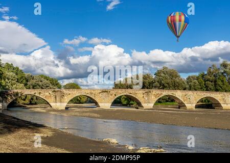 A colorful hot air balloon flies over the ancient Buriano Bridge, Arezzo, Italy Stock Photo