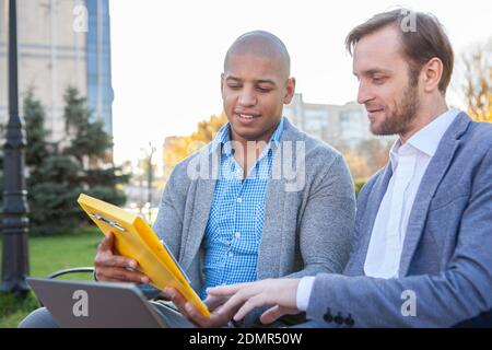 Two male colleagues discussing their startup outdoors, copy space. Business coworkers meeting to discuss their project Stock Photo