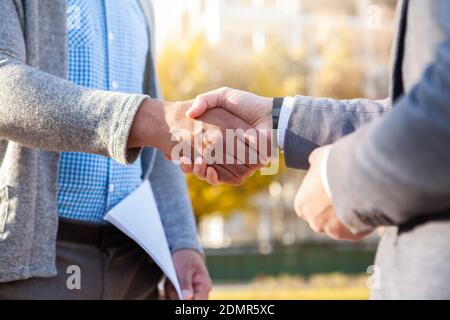 Cropped close up of two male colleagues shaking hands outdoors. Unrecognizable businessmen shaking hands in the park Stock Photo